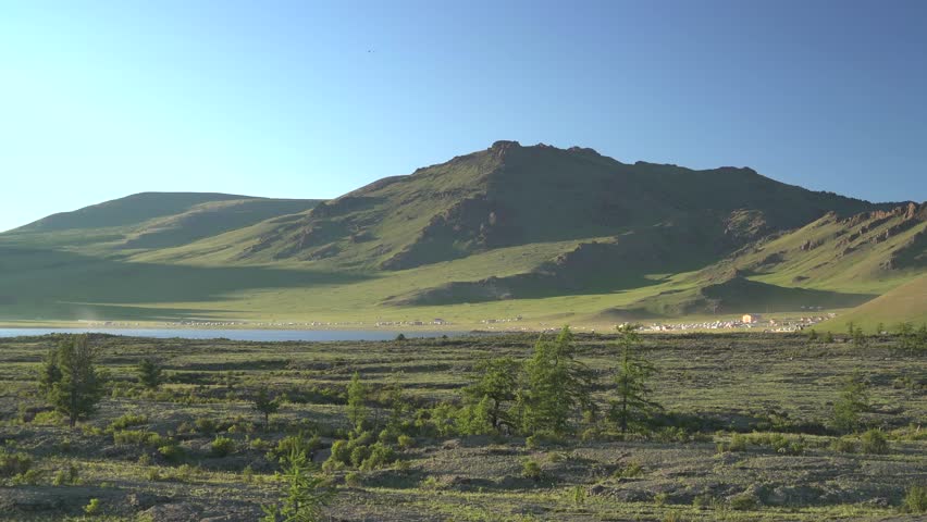 Panoramic view of Central Asia lakeside basalt plain with frozen lava rocks and volcanic terrain. Solidified magma meets quiet water, barren steppe, remote dawn atmosphere, earth science. Dark basalt fragments and pale lakeside light create a strong earth science subject with clear mineral texture. The footage can support searches for volcanic terrain, rugged shore, central Asian steppe, ancient lava, geologic formation, and wilderness panorama. The open composition also works as a natural background for environmental and exploration themes.