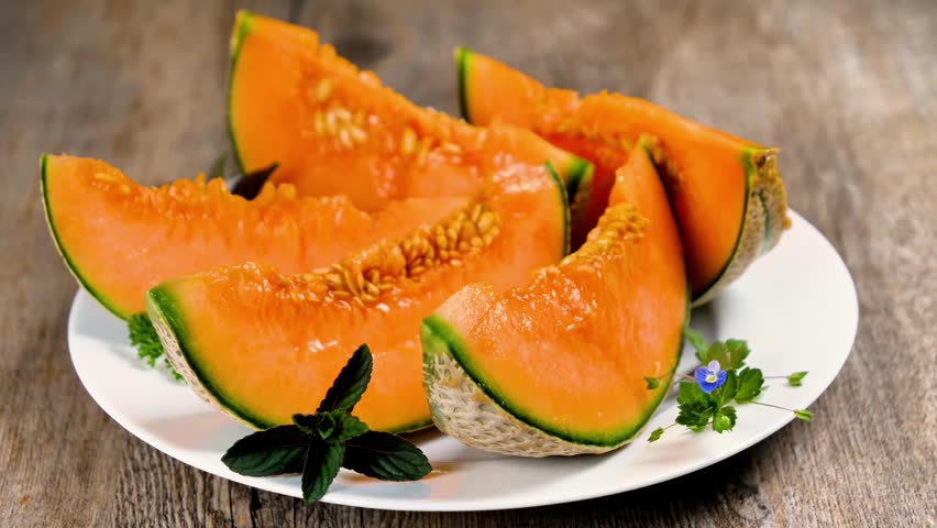 Slices of fresh cantaloupe melon served on white plate over rustic wooden table