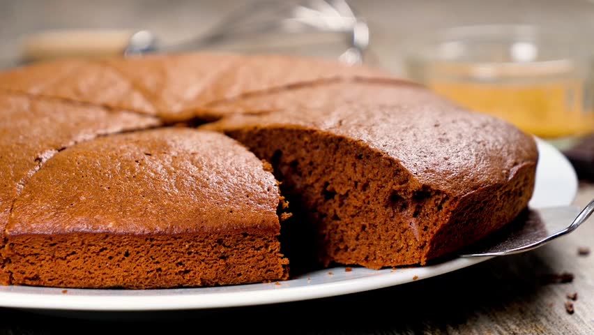 Slices of homemade chocolate cake served on white plate with baking utensils in background