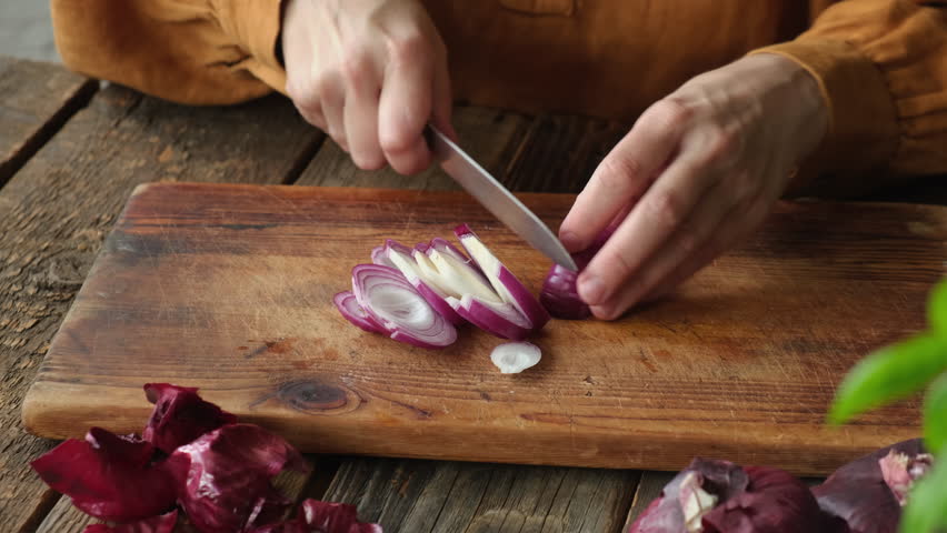 Hands slice red onion on wooden board. Cooking food process, meal prep. 