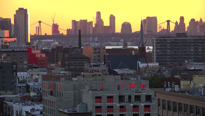 Cinematic footage of vibrant sunset over new york city skyline featuring manhattan bridge silhouetted against golden sky with urban buildings in foreground and bustling metropolis atmosphere.