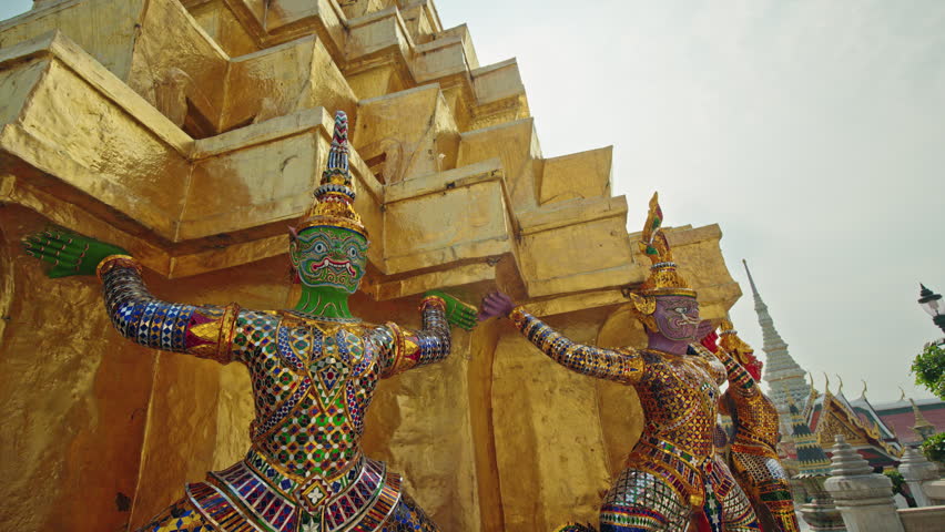 Guardian demon statues supporting golden stupa at Wat Phra Kaew in Bangkok, colorful Thai temple architecture in Thailand.