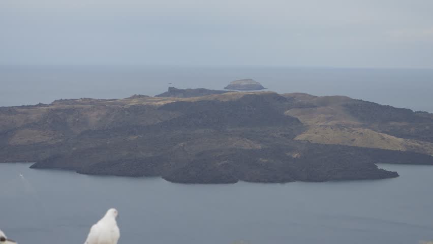 Pan across the Santorini caldera with Tholos Naftilos and pigeons in the foreground, Greece.