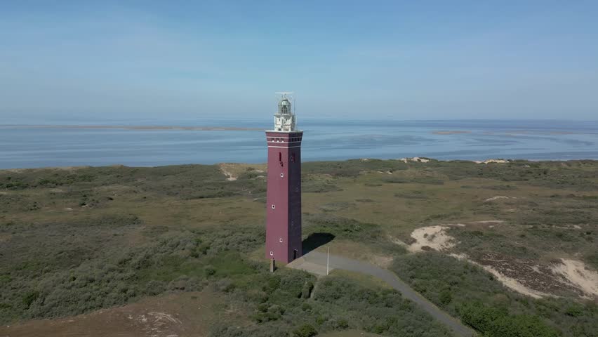 The reddish-brown Westhoofd Lighthouse in the province of Zuid Holland in the Netherlands towers like a lonely sentinel above the dune landscape.