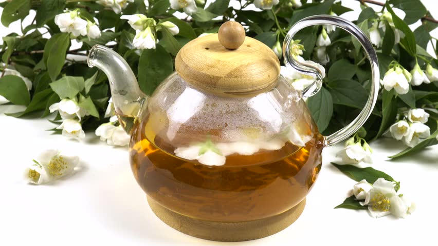 Tea with aroma philadelphus in transparent glass teapot against the backdrop of bunch of fresh philadelphus flowers is on a white table 