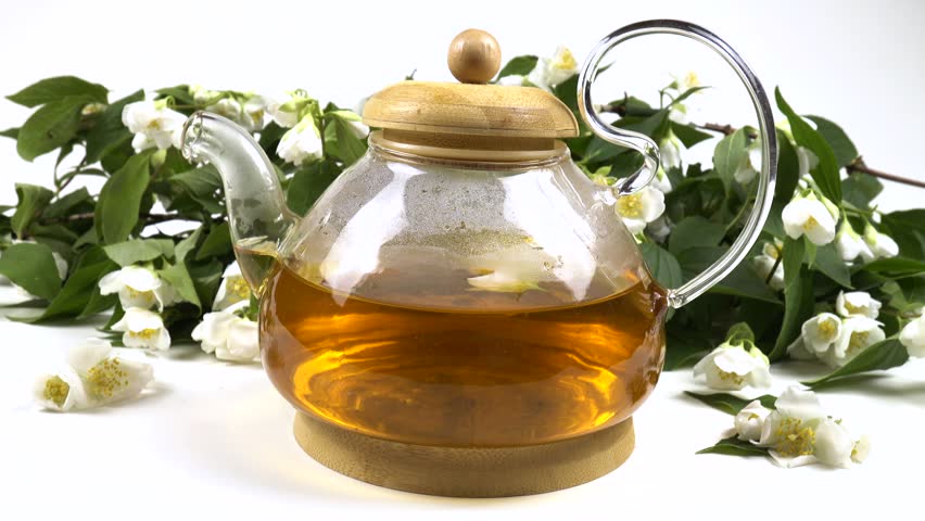 Tea with aroma philadelphus in transparent glass teapot against the backdrop of bunch of fresh philadelphus flowers is on a white table 
