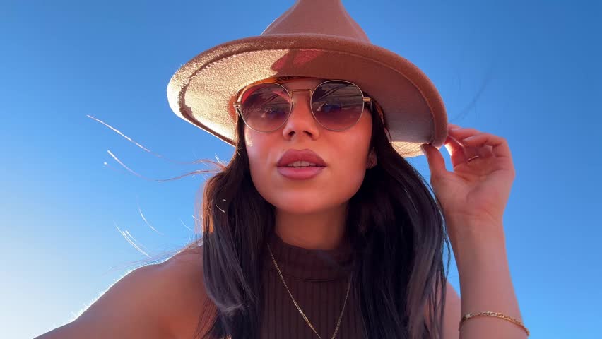 Stylish young woman wearing a hat and sunglasses filming herself with a smartphone, showing the breathtaking panorama of horseshoe bend on the colorado river in page, arizona