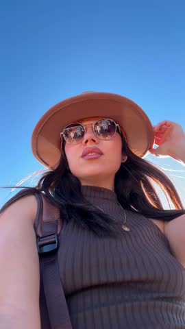 Stylish young woman wearing a hat and sunglasses taking a selfie video, revealing the spectacular horseshoe bend on the colorado river in page, arizona, on a sunny day of exploration