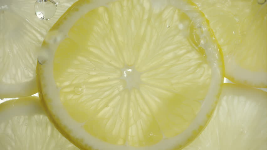 Drops of liquid falling on fresh sliced lemon pieces in slow motion. Beautiful ice water splash on lemon slices in macro. Vitamin C or serum acid in cosmetic product
