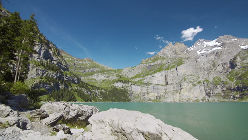 Mountain lake with a rock in the foreground, surrounded by forested slopes and snow-capped peaks