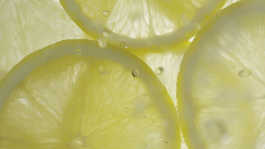 Drops of liquid falling on fresh sliced lemon pieces in slow motion. Beautiful ice water splash on lemon slices in macro. Vitamin C or serum acid in cosmetic product