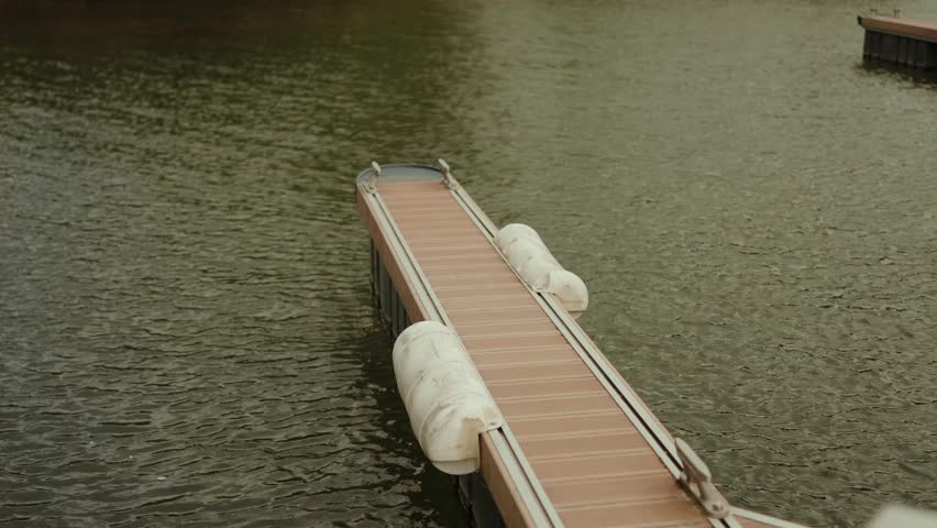 Floating wooden pontoon dock with white fenders moored on calm river water
