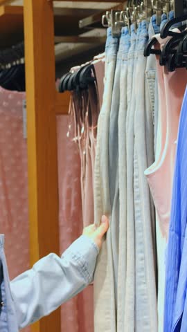 Closeup of hands browsing shirt display. Customer carefully reviews fabric details on clothing rack. Individual inspecting and adjusting hangers on vibrant clothing display in store