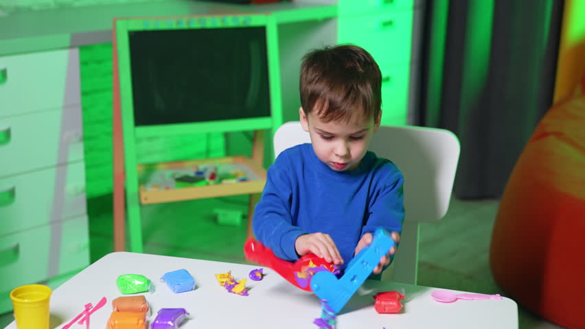 Cute Caucasian toddler cleans molding machine from plasticine. Baby boy sculptures for play dough.