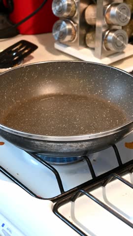 Close up of a hand cracking a fresh egg into a nonstick pan for breakfast on a gas stove