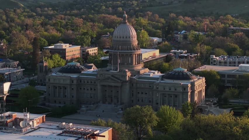 Boise, Idaho – USA – May 1, 2026: Elegant slow orbit drone shot circling the majestic Idaho State Capitol building in Boise during beautiful early spring morning light. Soft golden sunlight gently illuminates the iconic gold-leaf dome and grand neoclassical architecture. Peaceful spring atmosphere with clear skies and fresh greenery. Perfect for travel, government, historic landmarks, city pride, and cinematic aerial footage.
