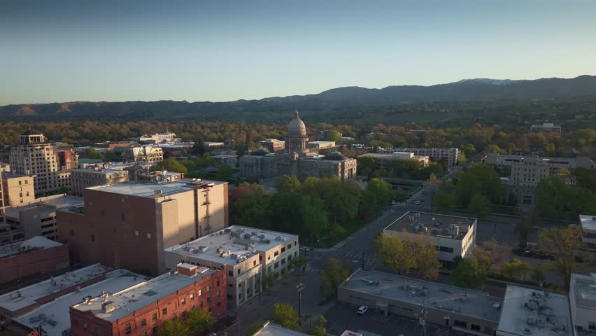 Boise, Idaho – USA – May 1, 2026: Elegant wide-angle slow orbit drone shot circling the majestic Idaho State Capitol building in Boise during beautiful early spring morning light. Golden sunlight illuminates the iconic gold-leaf dome and grand neoclassical architecture. Peaceful spring atmosphere with clear skies and fresh greenery. Perfect for travel, government, historic landmarks, city pride, and cinematic aerial footage.