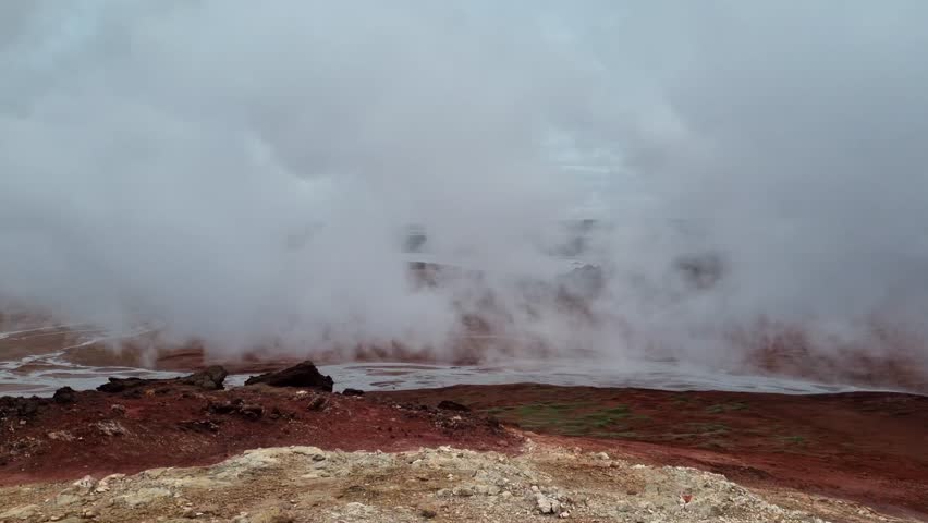 Geothermal field in Iceland with hot springs and fumaroles. Volcanic landscape covered with rising steam from the hot, red ground