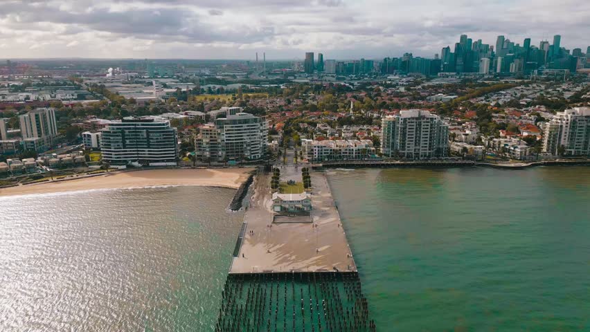 Scenic aerial footage showcasing Princes Pier, waterfront homes, the Melbourne CBD and expansive coastal scenery during a sunny windy morning.