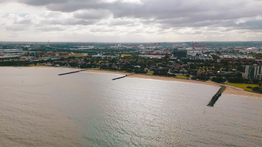 Cinematic 4K drone footage capturing Port Melbourne Beach, Sandridge Lookout, and calm ocean waters beneath cloudy morning skies.