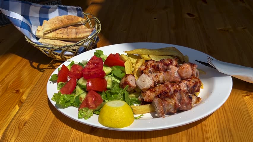 A large plate at a Greek restaurant: grilled pork souvlaki, vegetable salad, grilled potatoes, and pita bread. Greek fast food, a delicious dish – gastronomic tourism