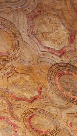 Vertical close-up of an ornate Pompeii ceiling with circular medallions, faded fresco color, and preserved decorative plaster from an ancient Roman interior.