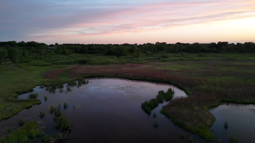 Aerial drone footage over a natural wetland pond and green vegetation at Saylorville Lake near Des Moines Iowa at dusk with colorful sunset sky above