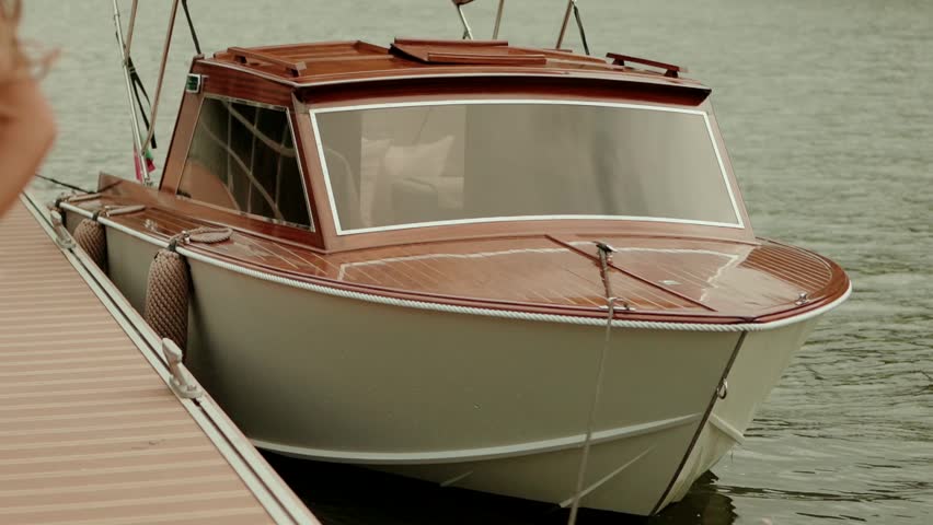 Classic vintage wooden motorboat with cabin moored at floating dock on calm grey river water