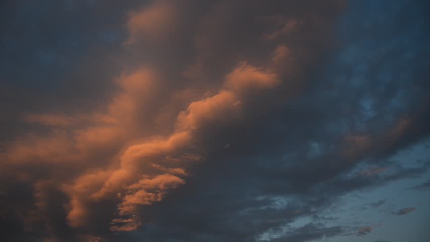 Dramatic sunset sky with glowing clouds over a mountains landscape. Golden light illuminates textured clouds, creating a powerful contrast with the dark blue sky.