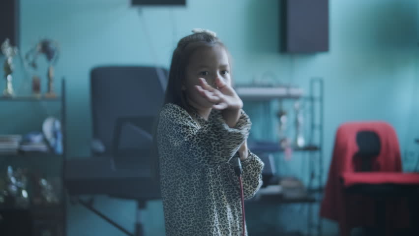 Little girl singing into a microphone during a vocal lesson with a teacher in a music studio.