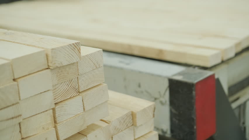 A neat stack of wooden boards on a pallet with a blurred person operating an automated line in the background
