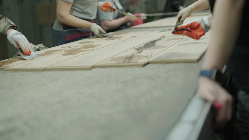A neat stack of wooden boards on a pallet with a blurred person operating an automated line in the background