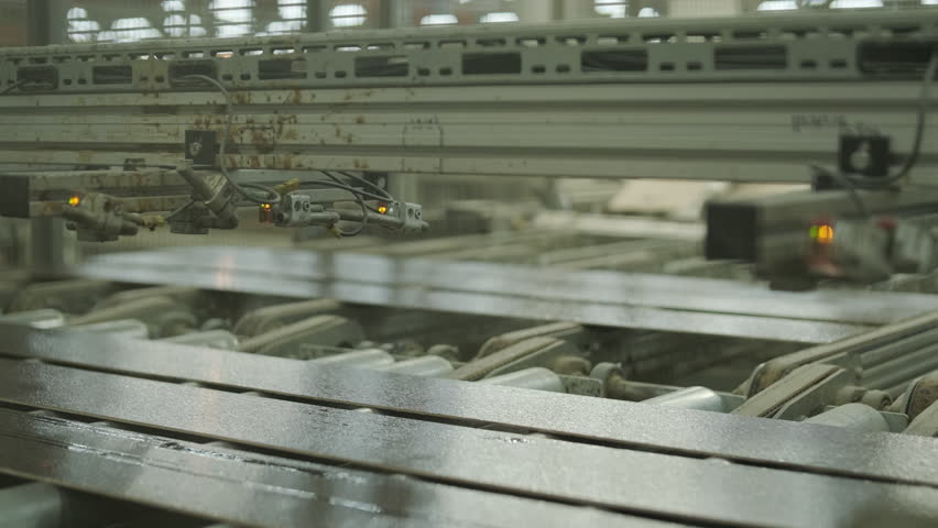 A neat stack of wooden boards on a pallet with a blurred person operating an automated line in the background