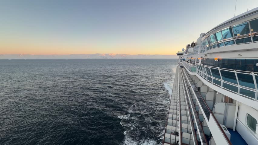 Epic Antarctica Cruise Ship At Sunset. Wide Shot Of Starboard Side of the Boat, Calm Ocean, Orange Sky with Glaciers and Snowcapped Mountains