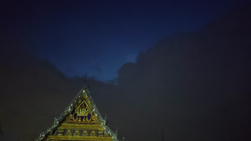 A dark rain cloud with intermittent flashes of lightning in the night sky.