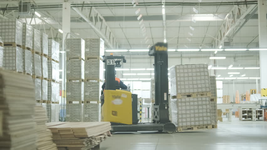A large industrial warehouse featuring a forklift operating among stacks of dried wooden planks prepared for further furniture or flooring production
