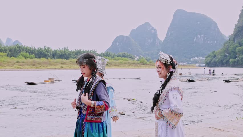 Young chinese women wearing traditional ethnic minority costumes are dancing by the Li River in Yangshuo, with the stunning karst mountain landscape of Guilin in the background