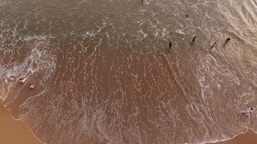 Aerial view of people standing in the shallow water as waves wash over the sandy shore in Galle, Southern Province, Sri Lanka.
