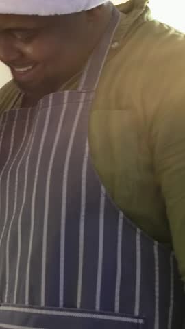 Vertical video: Camera panning, man leaning and smiling in kitchen, wearing Santa hat, making meal. Apron, couple, home, daylight, sunlit, dishrack, vertical video