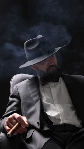 Mafia. Man smoking cigar in armchair against dark background. Camera moving right