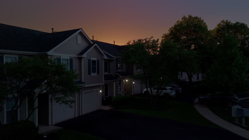 Drone Dramatic sunset with glowing orange sky and dark cloud silhouettes over suburban houses at dusk.
