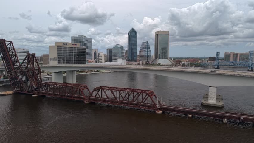 Aerial view of the Jacksonville skyline featuring the St. Johns River and historic bridges under a cloudy sky in Jacksonville, Florida, United States.