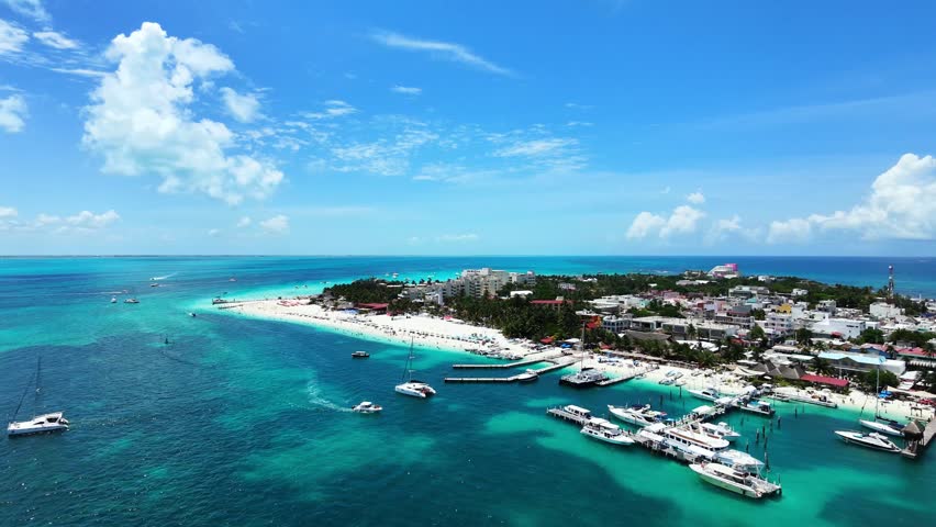 Wide aerial view flying forward toward Playa Norte in Isla Mujeres, Mexico. Smooth 4K 60fps drone shot showcasing a vibrant white sand beach, luxury yachts, and turquoise sea.