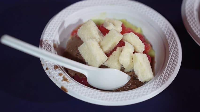 Indonesian ice dessert bowl with bread cubes, red jelly, avocado, and sweet syrup, colorful street food treat in close-up.