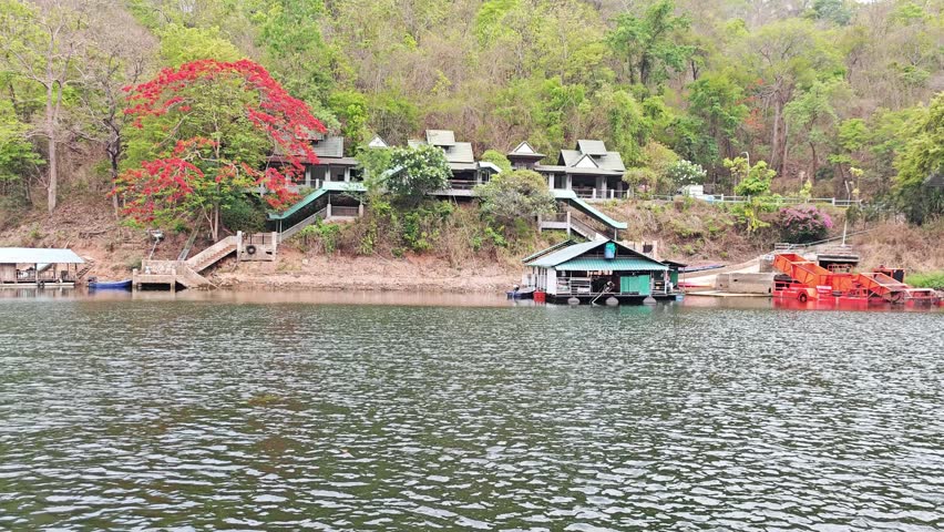 Tropical riverside resort with red flamboyant tree on hillside.