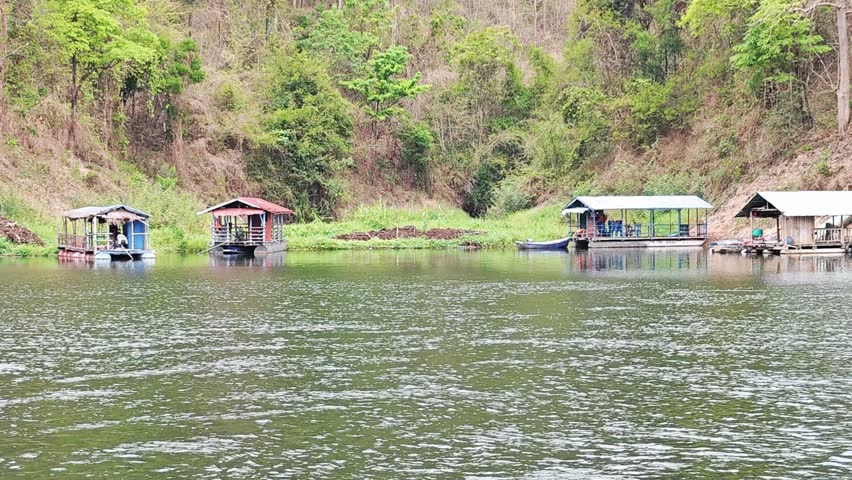 Floating raft houses along the riverbank in tropical forest.