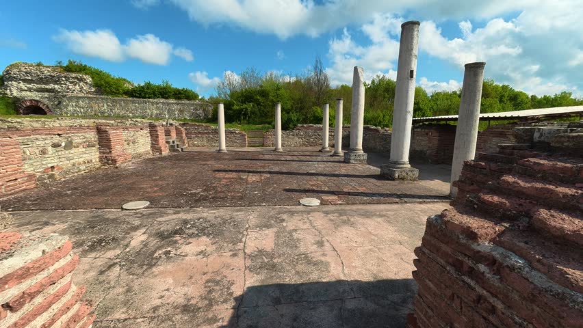 Ancient stone columns stand tall in open courtyard. Blue sky and clouds frame the historic ruins. Imperial Palace of Galerius, Felix Romuliana. Location: Serbia.