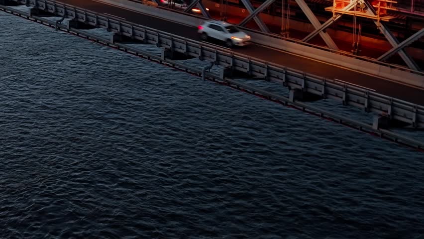 Direct top-down aerial view of vehicle lanes and industrial steel structure of the bridge at dusk.