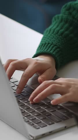 Close-up of hands typing on a laptop keyboard with focus on user interaction and computer input in a work or study environment with casual green sweater visible