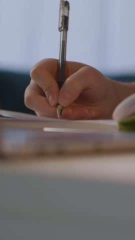 Close-up of a person writing with a pen on paper and a focused young woman concentrating, highlighting studying, note-taking, and deep thought activities in a quiet environment